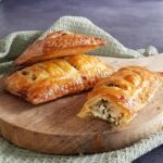 Spinazie feta broodjes van bladerdeeg. Uit één van de bladerdeegbroodjes is een hap genomen zodat je de vulling van feta en spinazie goed kunt zien.