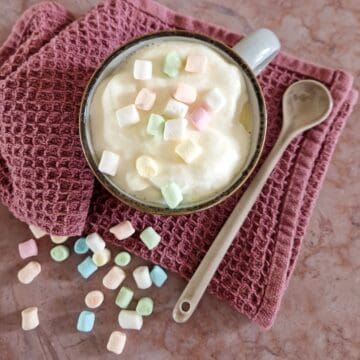 Een mok witte chocolademelk met marshmallows in verschillende kleuren.
