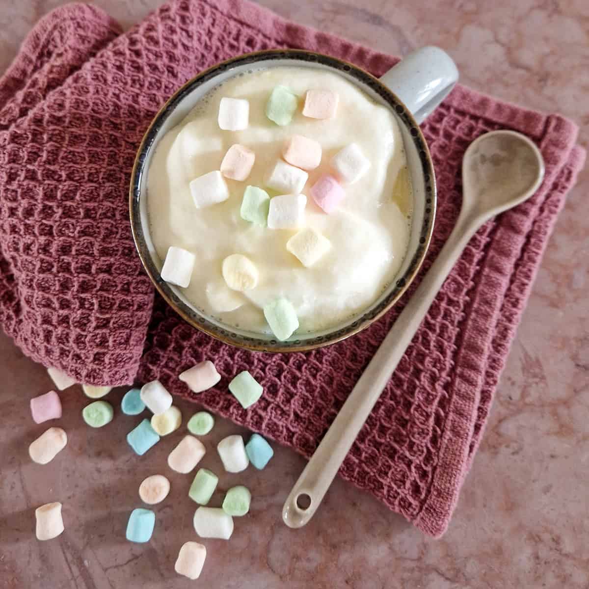 Een mok witte chocolademelk met marshmallows in verschillende kleuren.
