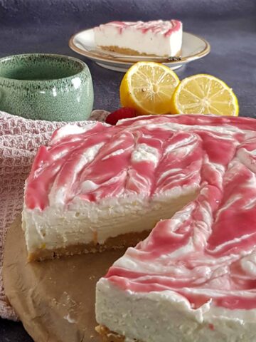 No bake kwarktaart op een stuk bakpapier. Er is een puntje uit de taart gesneden zodat je de afzonderlijke lagen van de kwarktaart goed kunt zien.