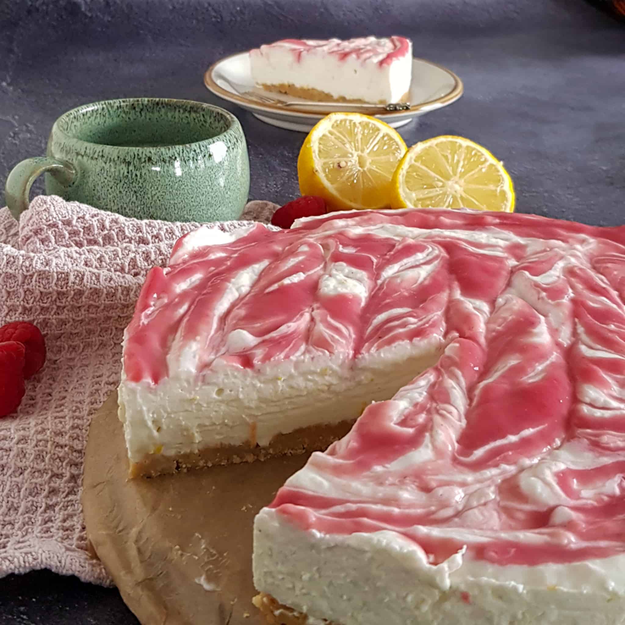 No bake kwarktaart op een stuk bakpapier. Er is een puntje uit de taart gesneden zodat je de afzonderlijke lagen van de kwarktaart goed kunt zien.