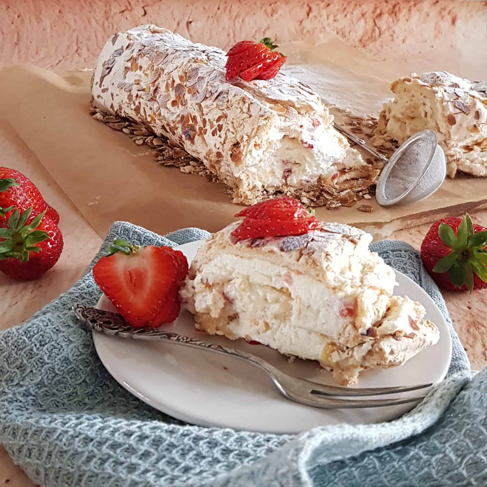 Aardbeien schuimtaart met amandelschaafsel. Een punt van de schuimrol ligt op een gebaksbordje. De taart is versierd met verse aardbeien.
