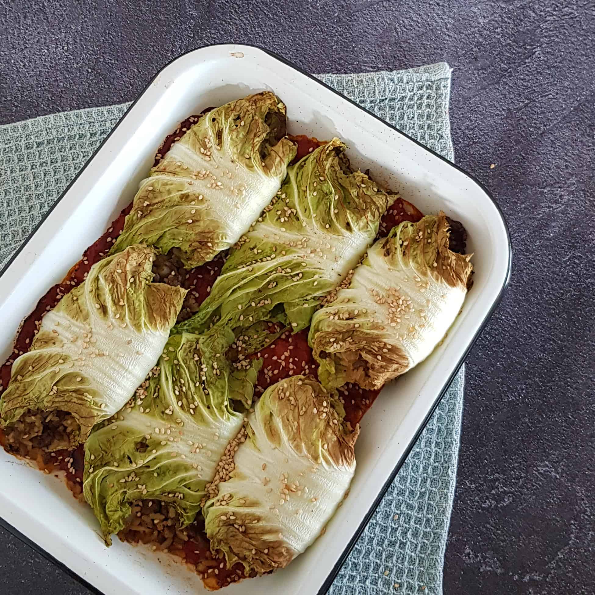 Gevulde koolrolletjes met rijst en gehakt in een tomatensaus. De rolletjes kool zijn bestrooid met witte sesamzaadjes.