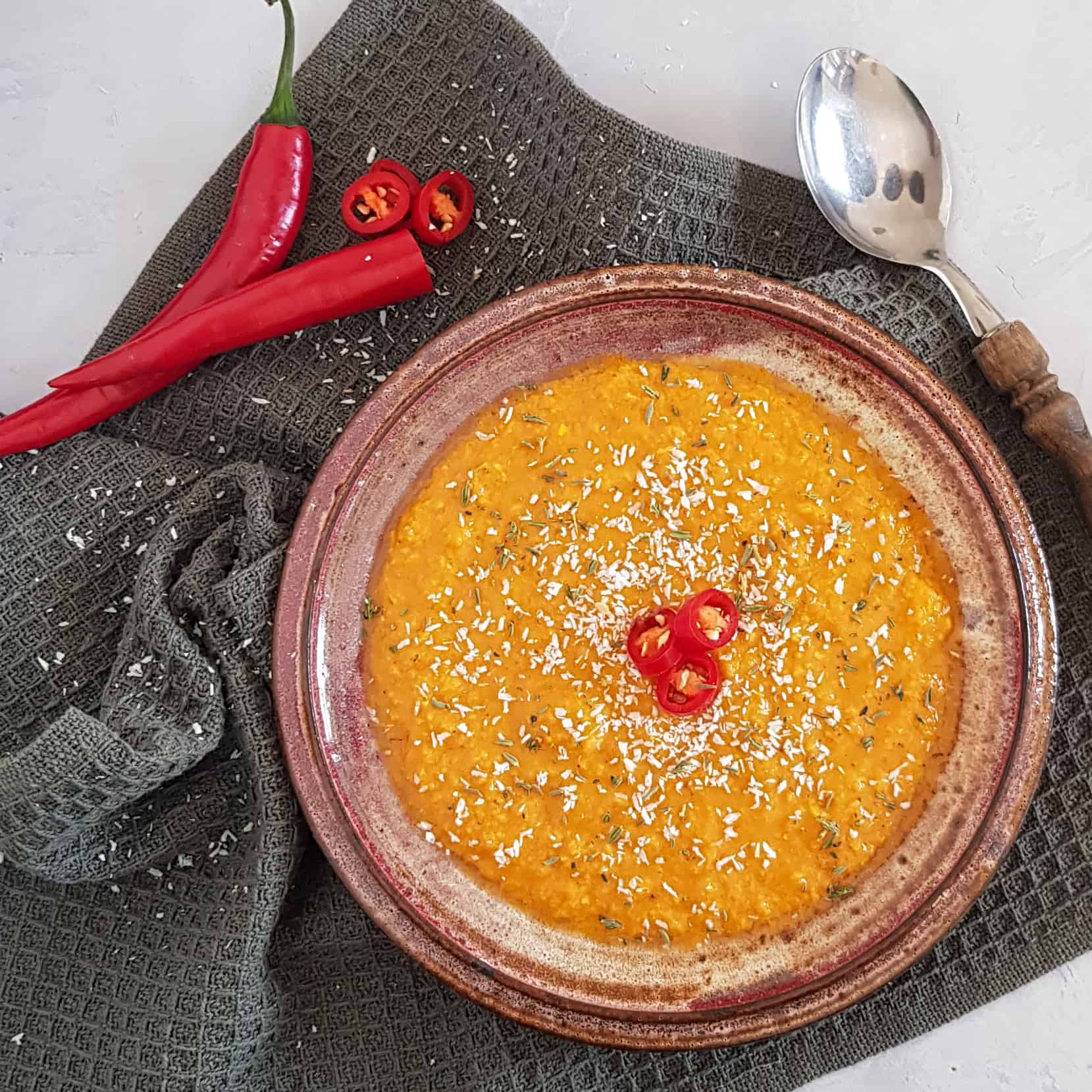 Currysoep in een ouderwets diep bord. De soep is bestrooid met kokosrasp en ringetjes rode peper.