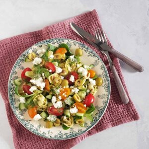 Pastasalade met feta, olijven, tomaat in verschillende kleuren en komkommer. De salade is gegarneerd met verse dille.