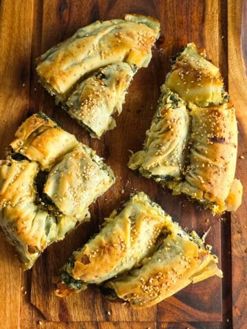 Spanakopita - quiche met spinazie en feta. Op een snijplank liggen vier stukken spanakopita.