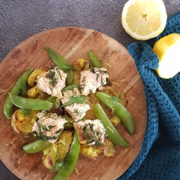 Zalm met krieltjes en peultjes op een houten plank. Het gerecht is bestrooid met citroenrasp en verse dille.