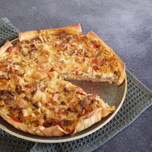 Prei shoarma quiche op een bord. Uit de quiche is een punt gesneden zodat de vulling zichtbaar wordt.