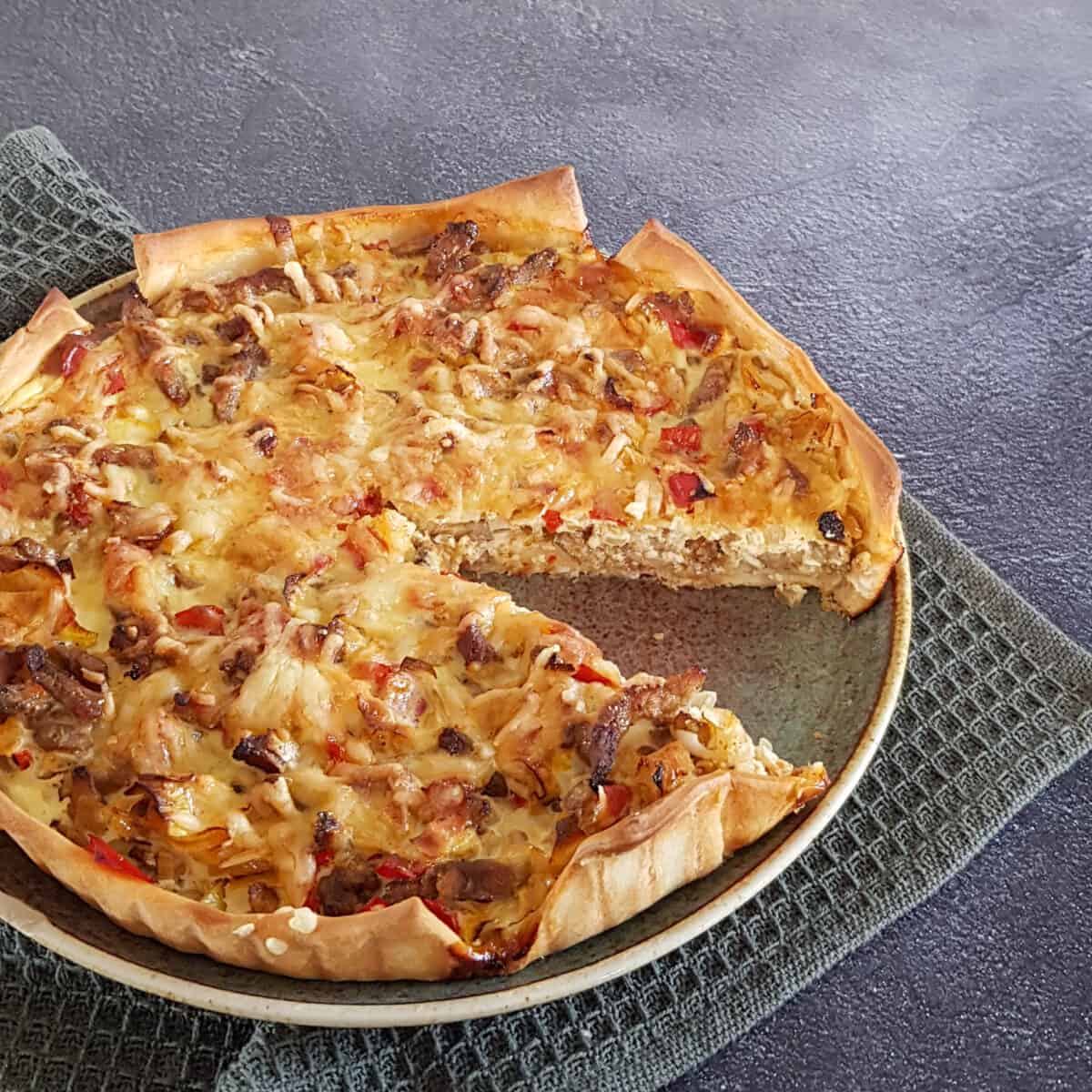 Prei shoarma quiche op een bord. Uit de quiche is een punt gesneden zodat de vulling zichtbaar wordt.