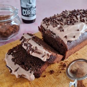 Chocoladecake met bier en roomkaasfrosting. De biercake is bestrooid met chocoladehagels en op de achtergrond staat een flesje bier.