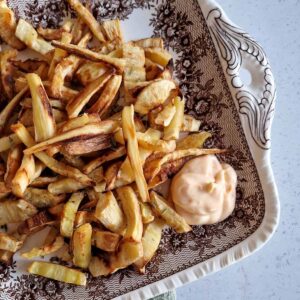 Pastinaakfrietjes op een ouderwets bord, met een klodder srirachamayonaise erbij om de friet in te dopen.