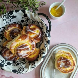 Zoete broodjes bakken met als resultaat een mandje vol zoete broodjes met lemon curd. Eén van de broodjes ligt op een gebaksschoteltje.