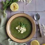 Brandnetelsoep recept met citroen en feta, in een ouderwets diep bord dat op een groene doek staat.