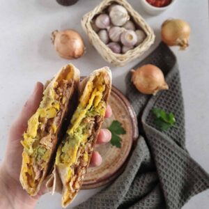 Een hand houdt gehalveer crunchwraps met kip omhoog, zodat de vulling van de wraps goed zichtbaar wordt.