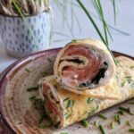 Close-up van een gevulde omelet wrap met spinazie en zalm. Het gerecht is bestrooid met veel verse bieslook.
