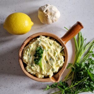 Knoflookboter maken met als ingrediënten boter, knoflook, citroen en veel verse kruiden.