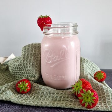 Een glas aardbeien drinkyoghurt met verse aardbeien ernaast.