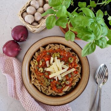 Een bord met pasta met tonijn, een basilicumplant, uien en knoflook.