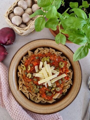 Een bord met pasta met tonijn, een basilicumplant, uien en knoflook.