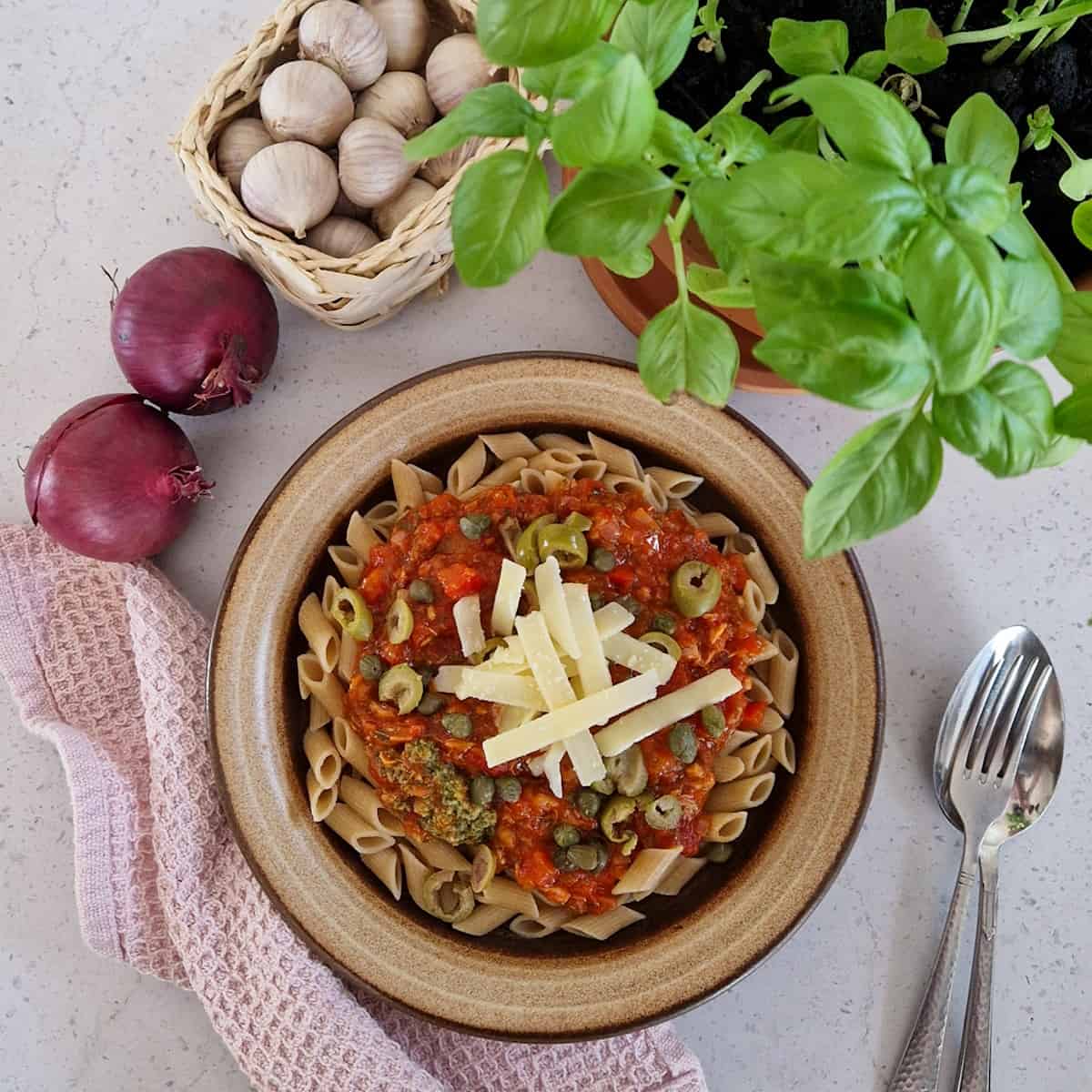Een bord met pasta met tonijn, een basilicumplant, uien en knoflook