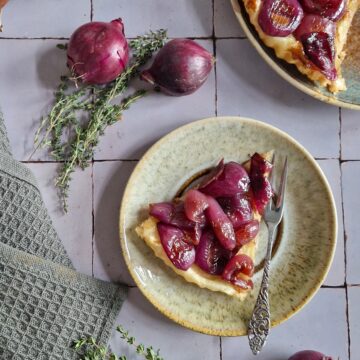 Een punt rode uien tarte tatin op een bordje, met uien en takjes tijm ernaast.