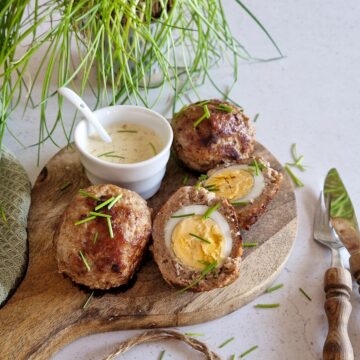 Een plankje met daarop drie Schotse eieren (gehaktballen gevuld met een gekookt ei), waarvan één gehalveerd.