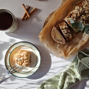 Een gevulde speculaasstaaf met amandelspijs op een stuk bakpapier en een gebaksbordje met een afgesneden stukje van de speculaasrol.