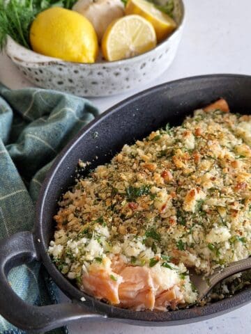 Een zalm met kruidenkorst in een zwarte ovenschaal.