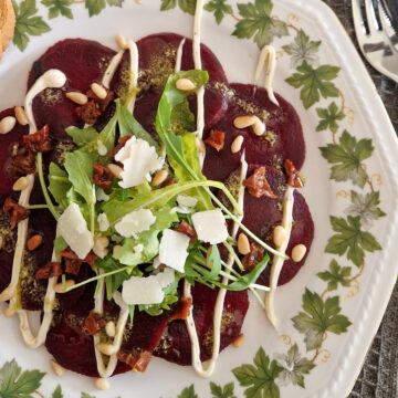 Een bord vegetarische carpaccio van rode biet met truffelmayonaise, sla en parmezaanse kaas.