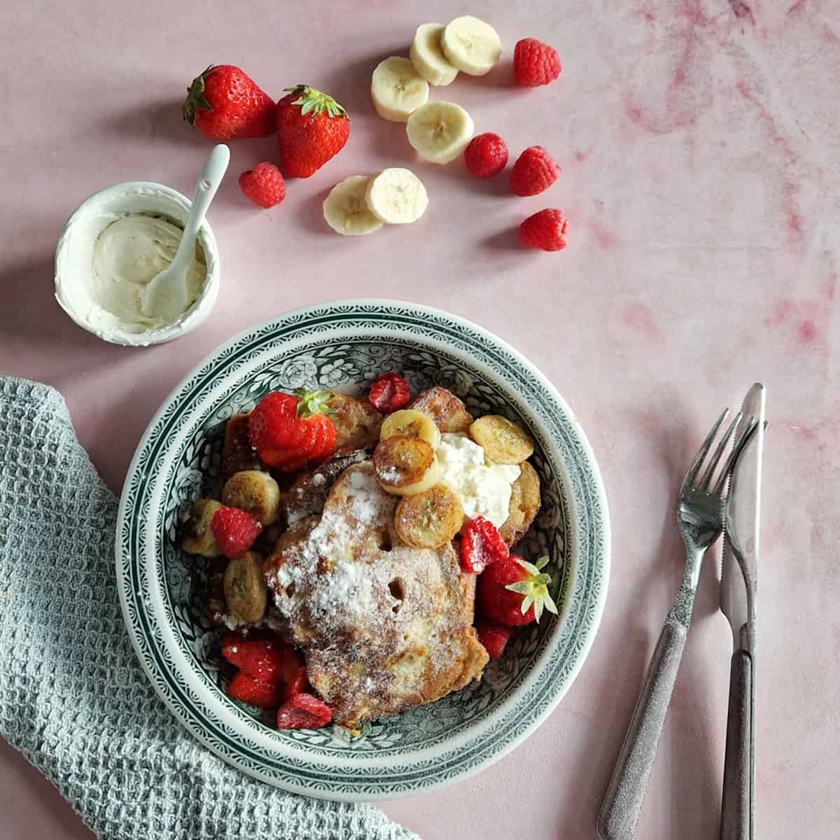 Een bord wentelteefjes van suikerbrood met gekarameliseerde banaan en aardbeien.