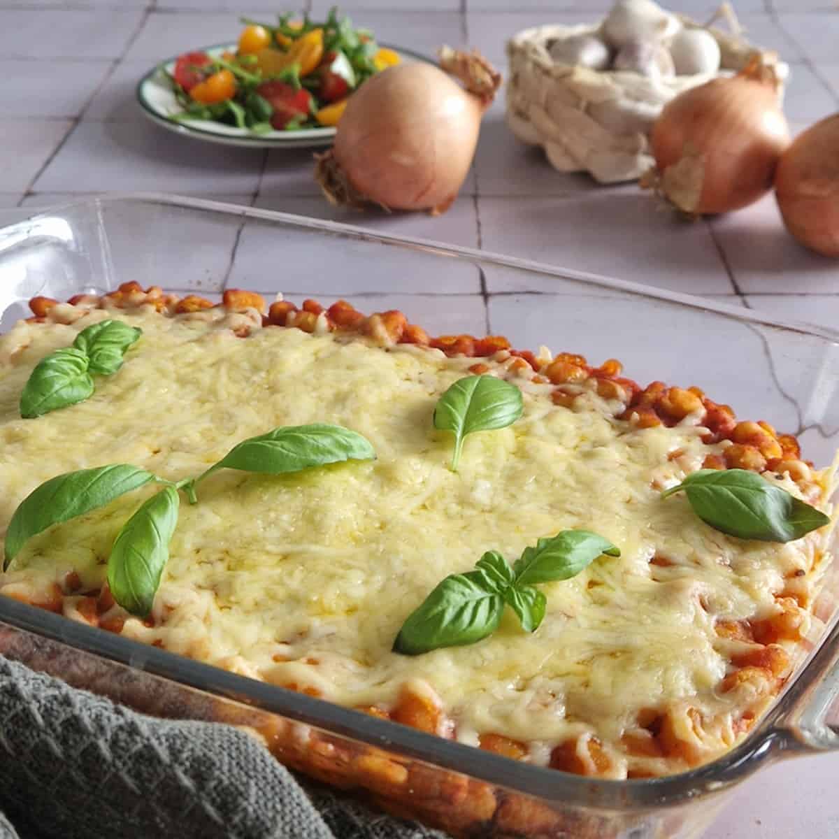 Witte bonen in tomatensaus in een ovenschotel. De bonenschotel is royaal bedekt met een laag geraspte kaas.