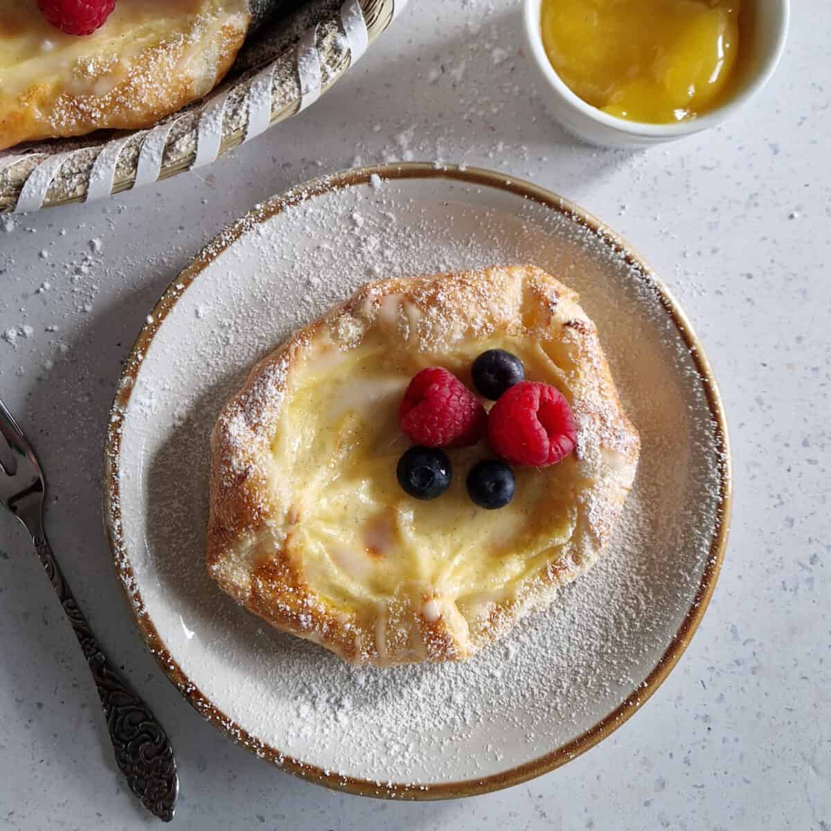 Deense broodjes met room op een gebaksbordje. Het zoete broodje is gegarneerd met vers fruit en poedersuiker.