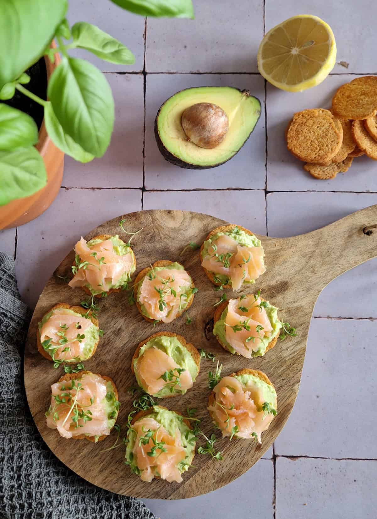 Een borrelplank met hapjes met gerookte zalm en een spread van avocado en doperwten.
