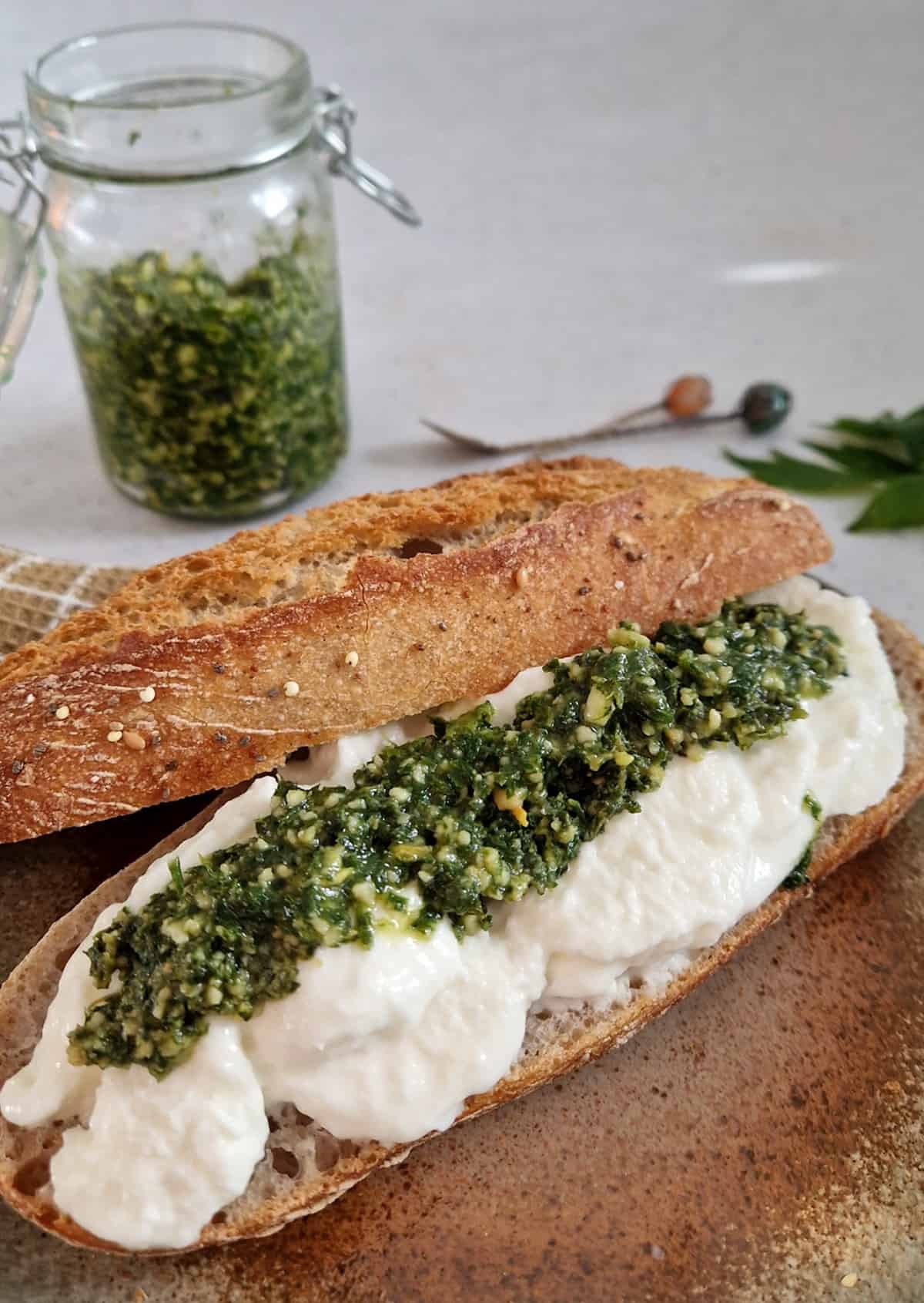 Een donkere pistolet met mozzarella en maggiblad pesto. Op de achtergrond staat een potje met de rest van de pesto.