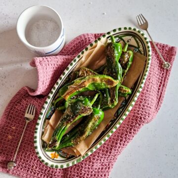 Een schaal met Pimientos de Padron, een tapas hapje van Spaanse groene pepers met zeezout. De schaal staat op een donkerroze doek en er liggen vorkjes op.