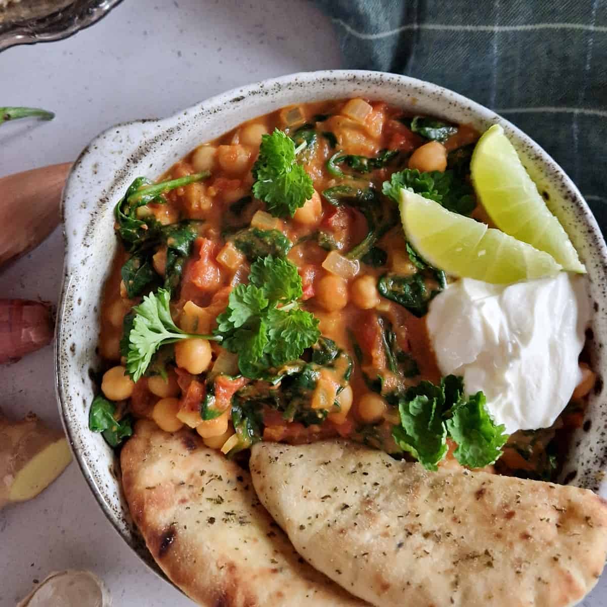 Een kom vegetarische kikkererwten curry met platbrood. De schotel is gegarneerd met verse peterselie en schijfjes limoen.