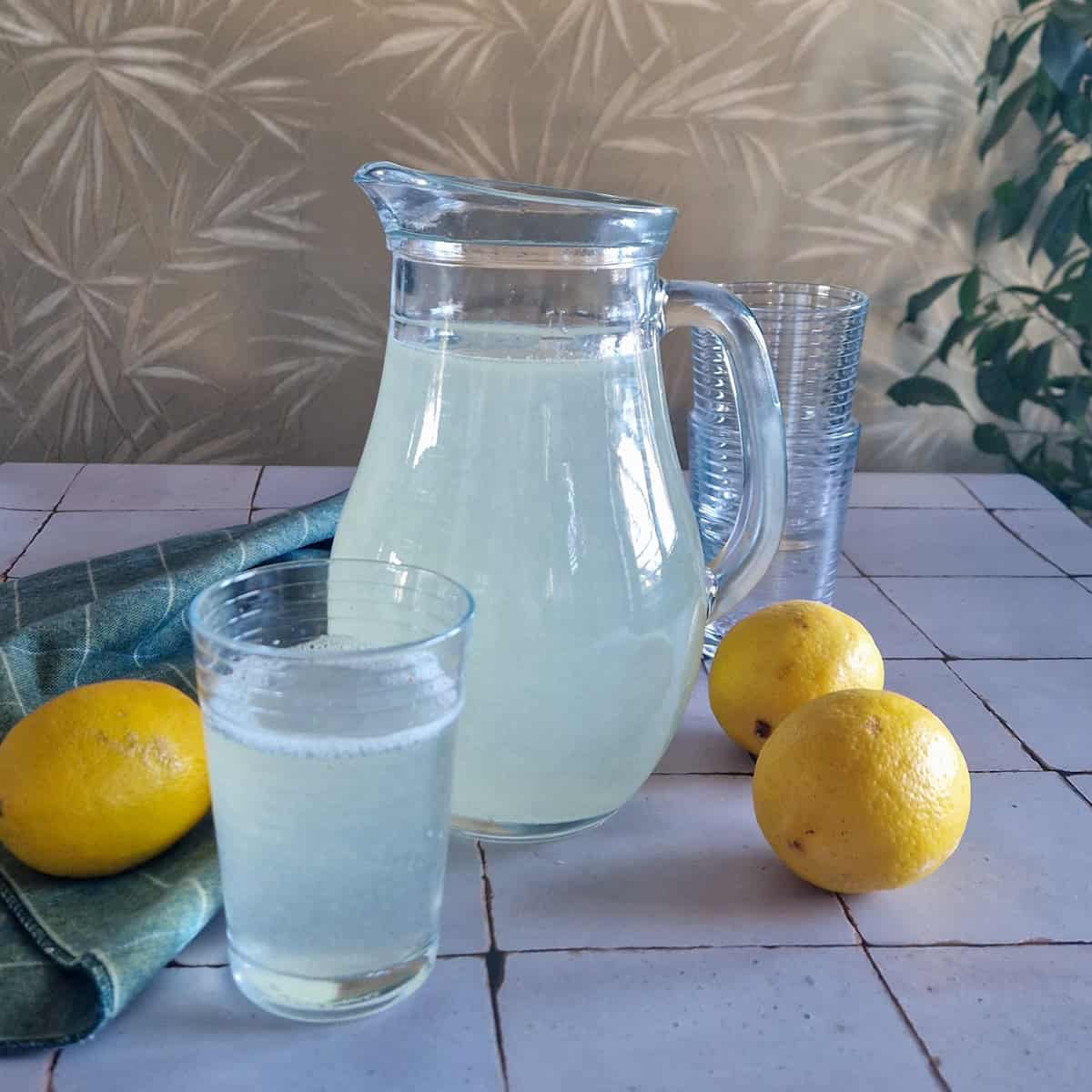 Een kan citroenlimonade met ernaast enkele citroenen.