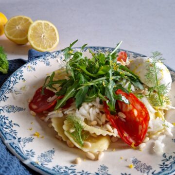 Een bord pasta met chorizo en venkel. De pasta is gegarneerd met rucola en op de achtergrond ligt een gehalveerde citroen.