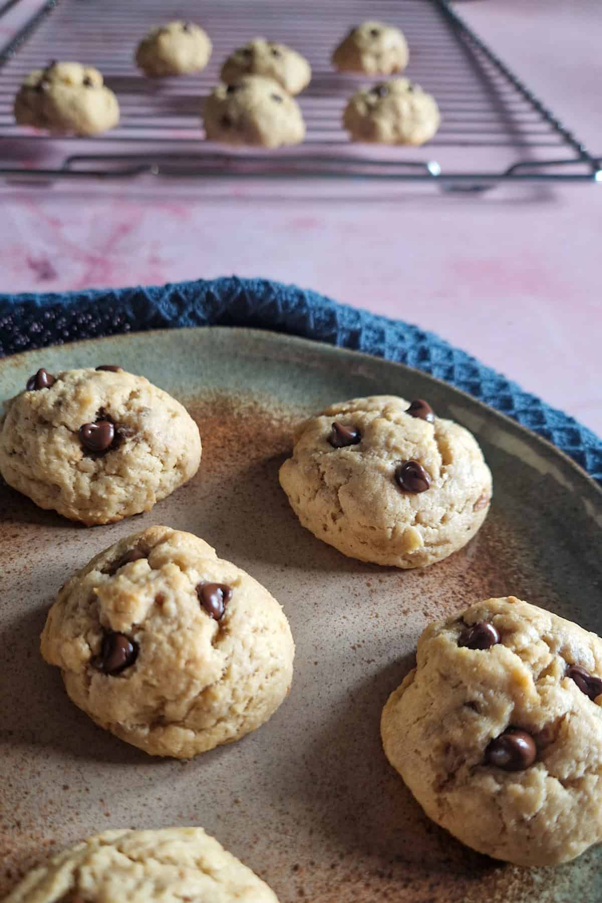 Suikervrije koekjes met pindakaas op een bord. Op de achtergrond liggen nog enkele koekjes op een rek af te koelen.