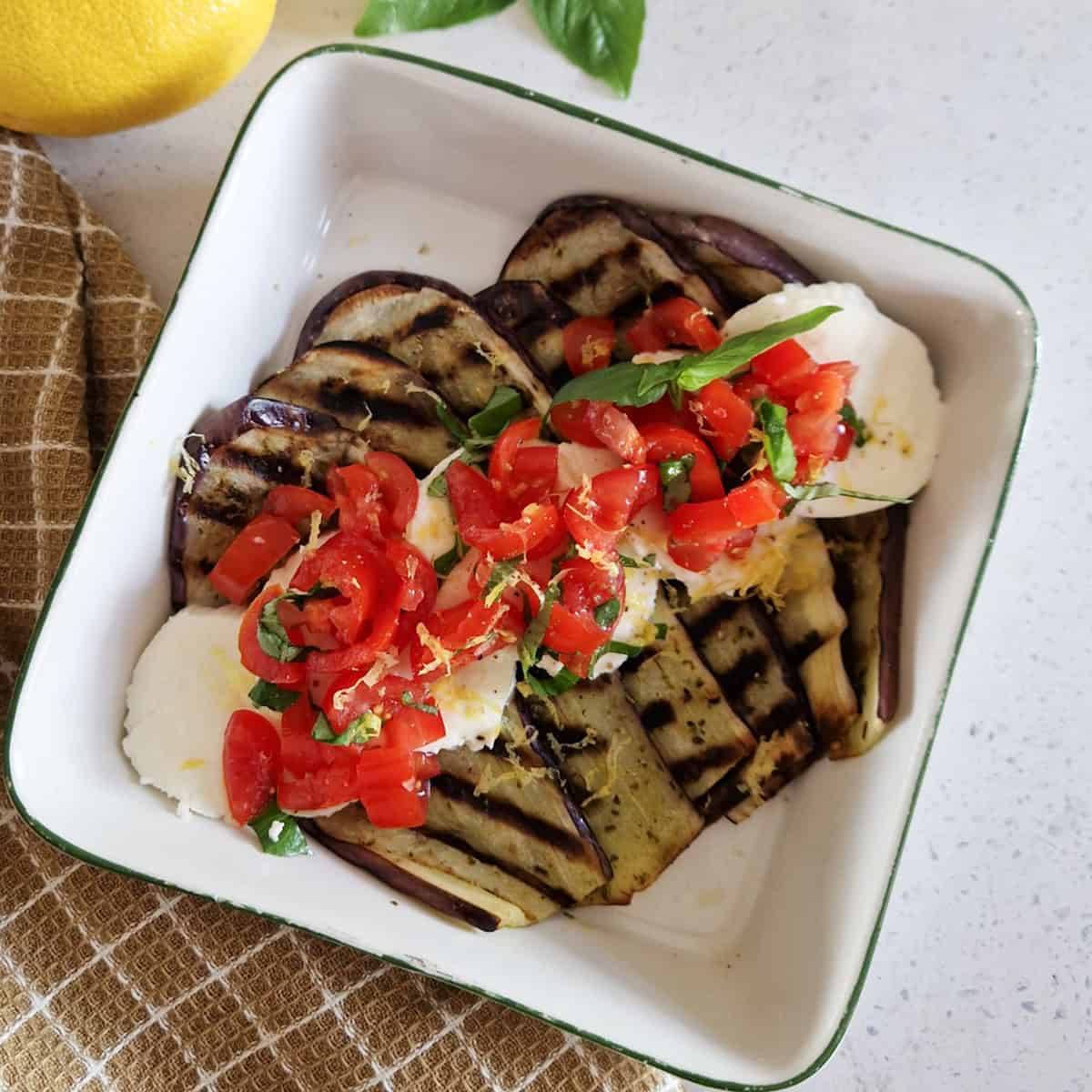 Een schaal gegrilde mozzarella met aubergine, fijngesneden tomaat en basilicum.