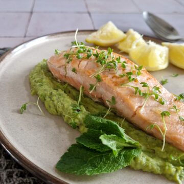 Een bord met knalgroene doperwtenpuree, met daarop een stukje net niet helemaal doorgebakken zalm. De zalm is gegarneerd met tuinkers.