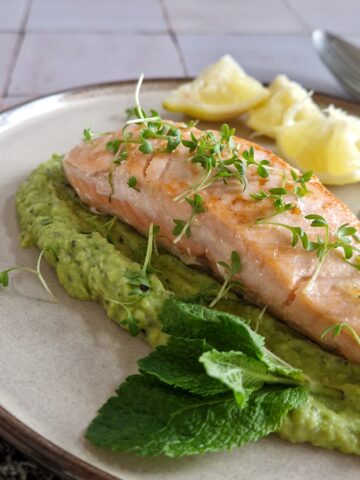 Een bord met knalgroene doperwtenpuree, met daarop een stukje net niet helemaal doorgebakken zalm. De zalm is gegarneerd met tuinkers.