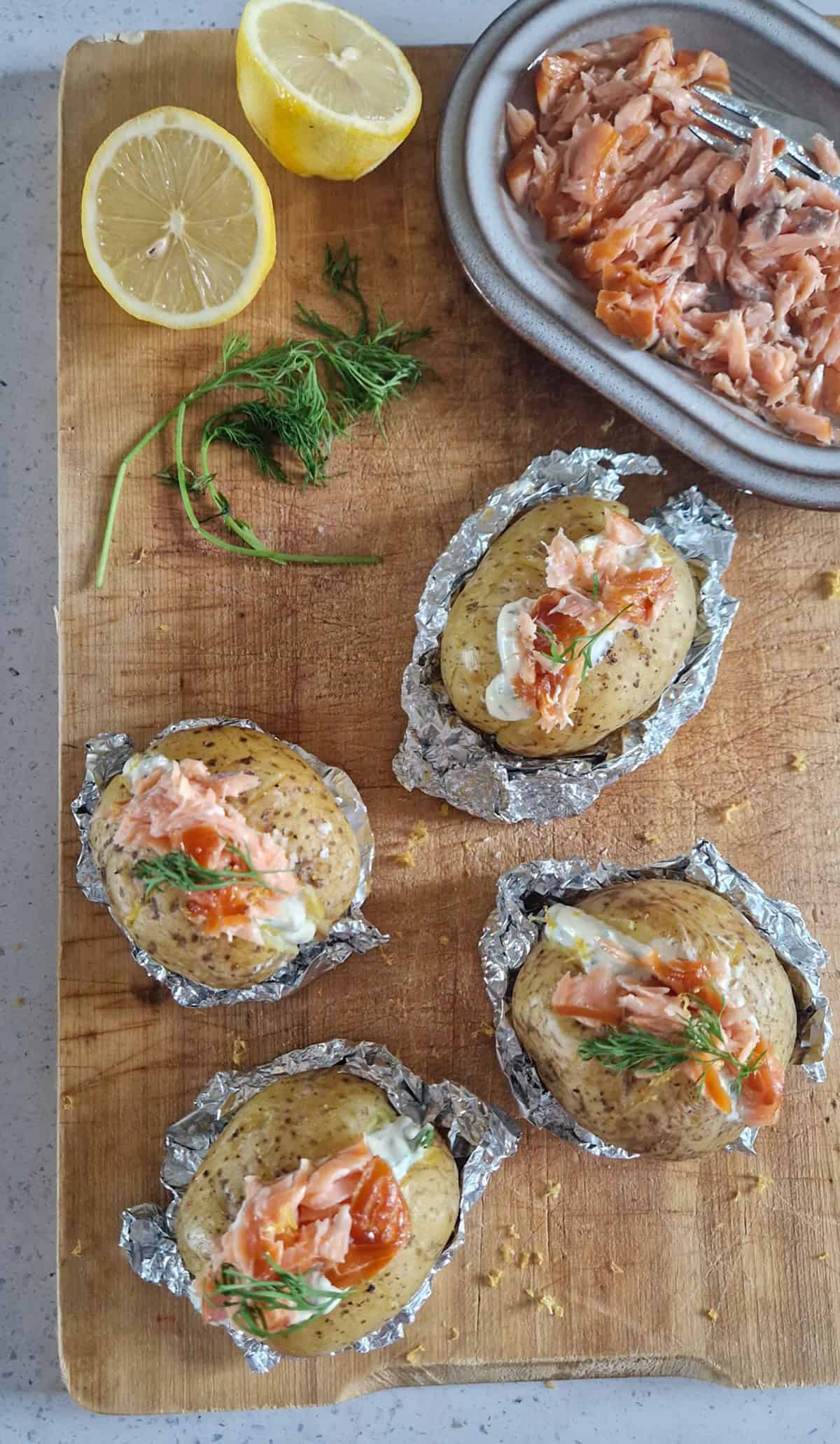 Warmgerookte zalm met aardappels op een houten serveerplank. Het gerecht is gegarneerd met verse dille.
