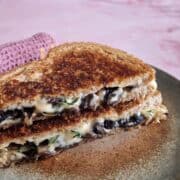 Vegetarische tosti met champignons, tijm en veel kaas. De tosti is schuin doormidden gesneden en de twee helften brood zijn op elkaar gestapeld.
