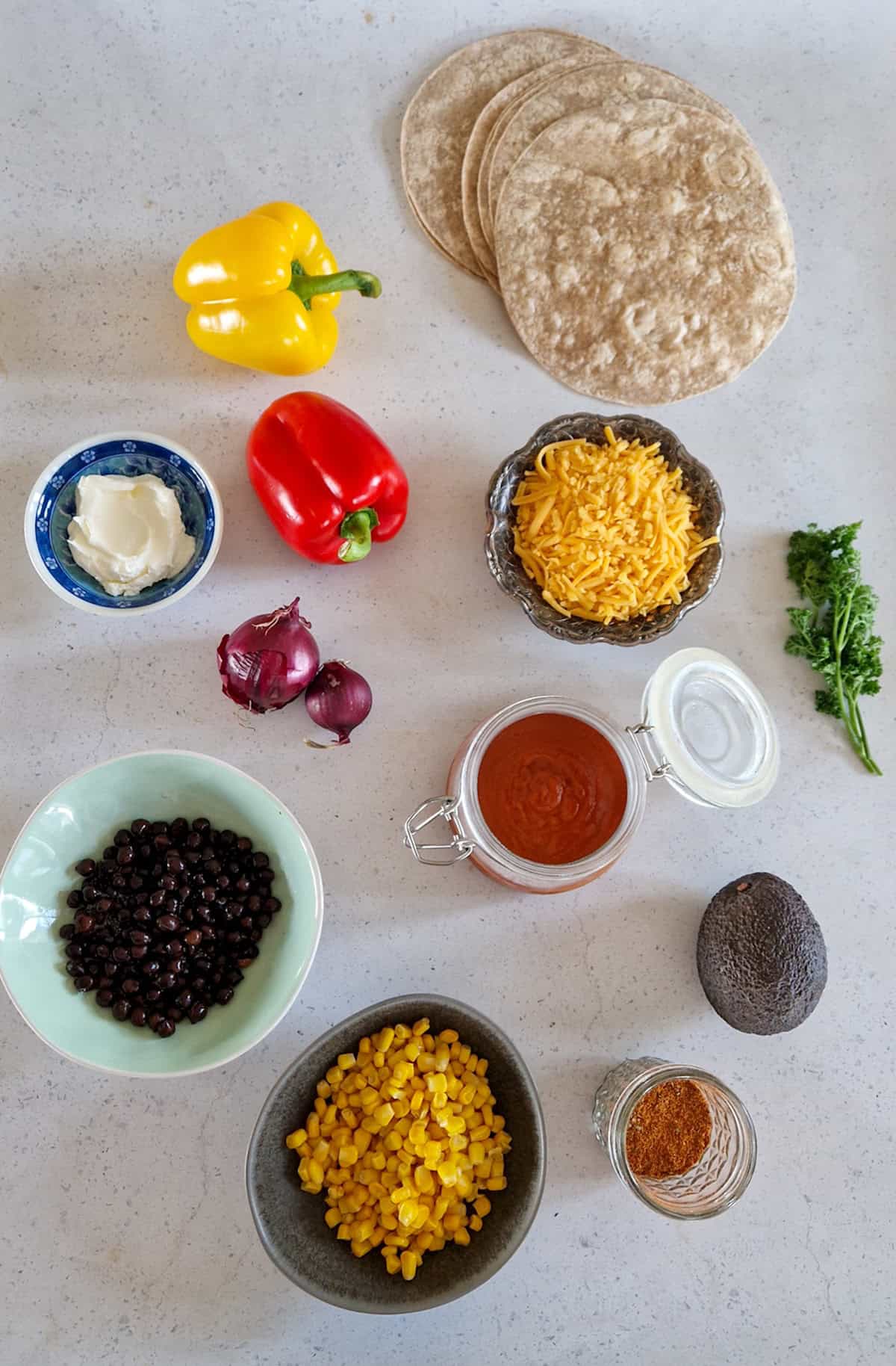 De ingrediënten om enchilada ovenschotel te maken, uitgestald op een witte ondergrond.