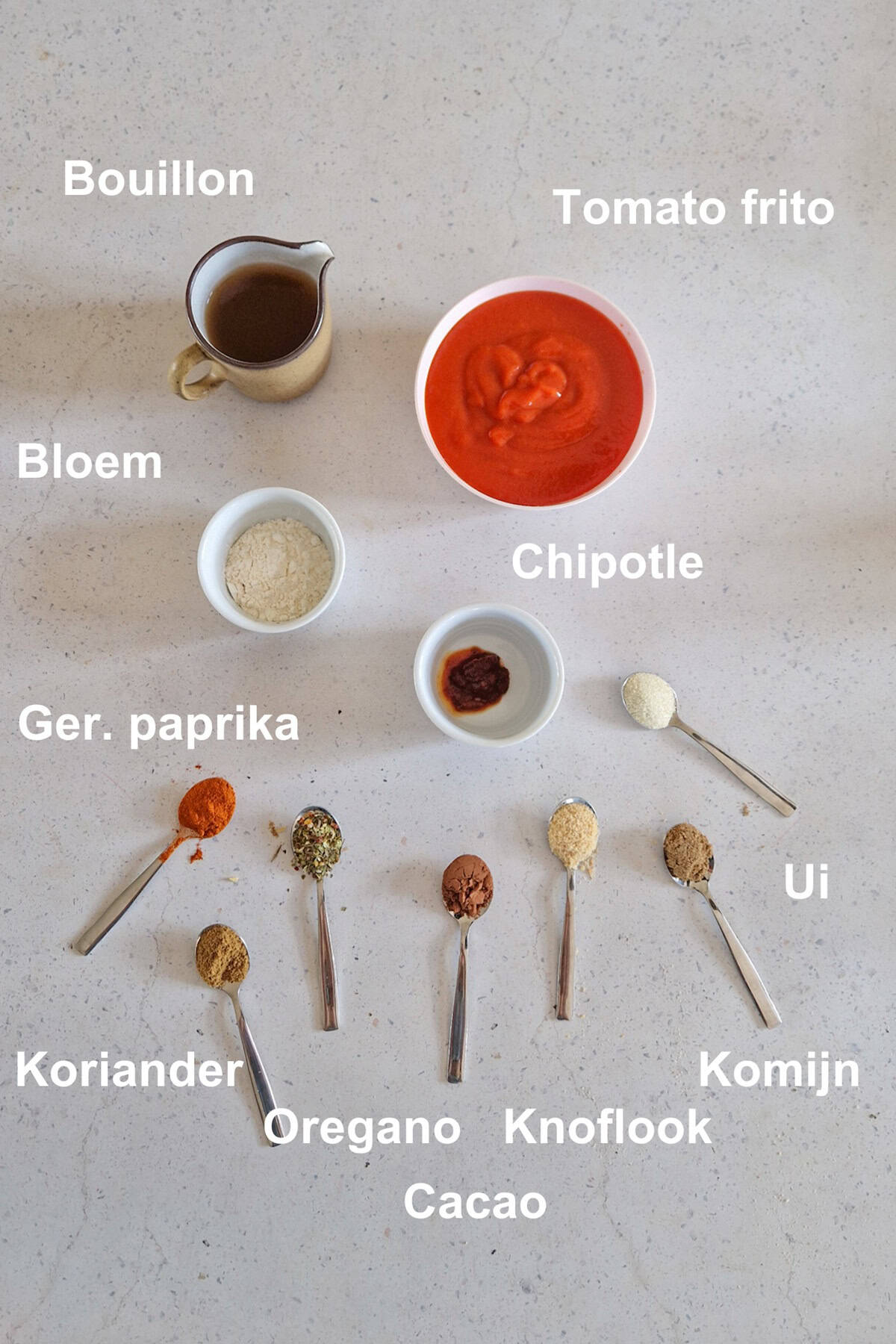 De ingrediënten voor rode enchiladasaus, uitgestald op een lichte ondergrond.