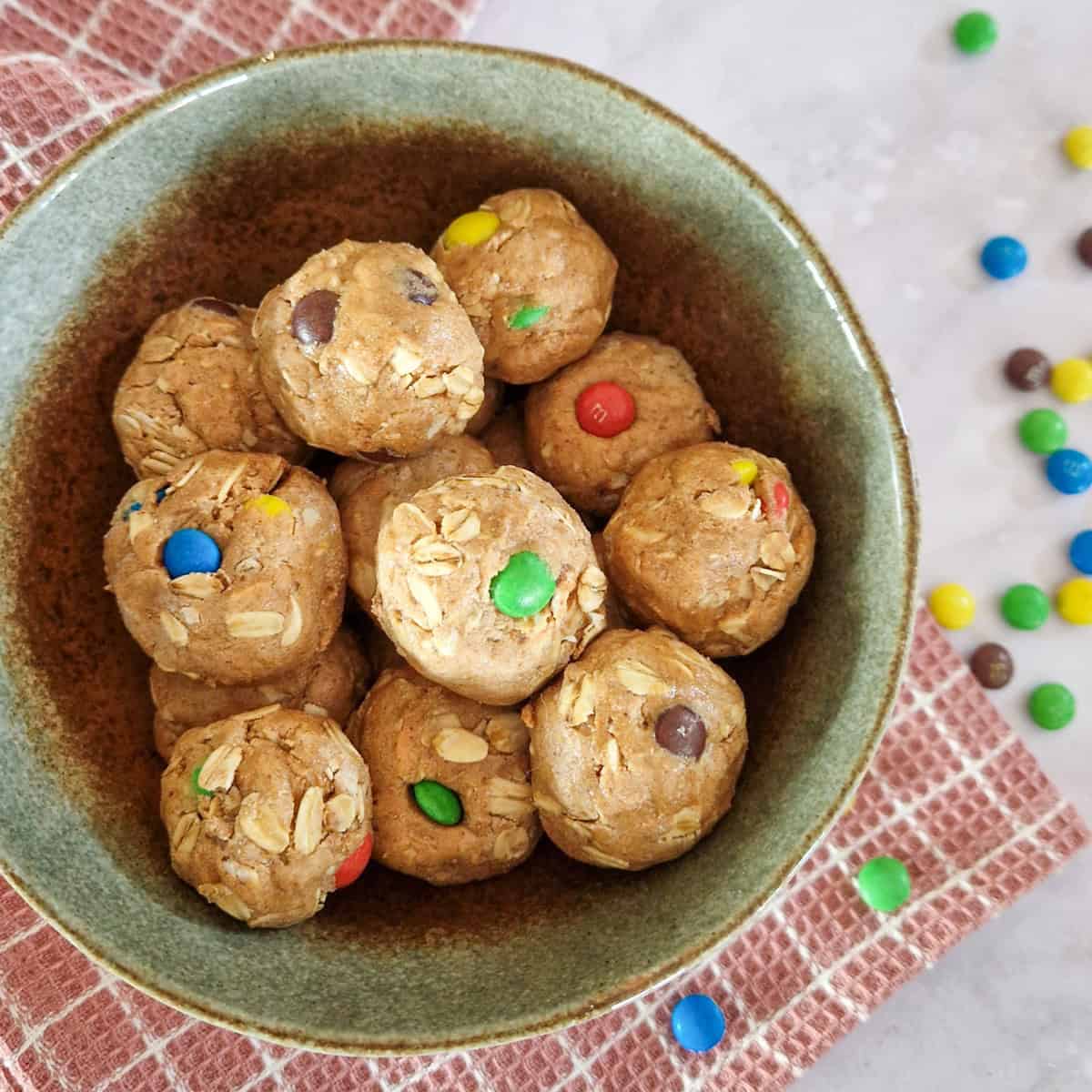 Een groen schaaltje gevuld met bliss balls. Je ziet enkele ingrediënten in de tussendoortjes zitten: pindakaas, havermout en mini M&M's.
