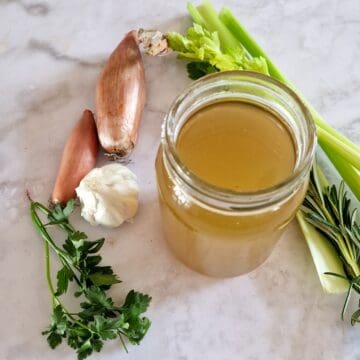Een glazen pot met zelfgemaakte groentenbouillon. Er omheen liggen enkele ingrediënten van de bouillon.