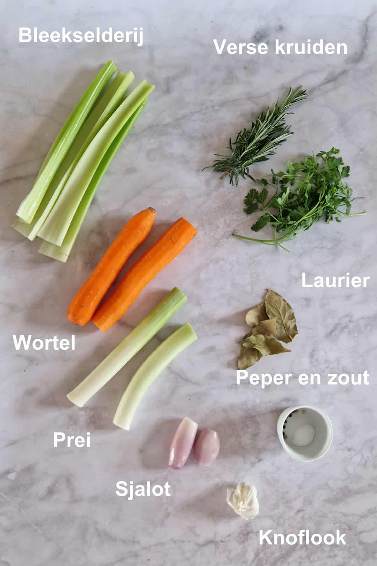 De ingrediënten om groentebouillon te maken, uitgestald op een marmeren ondergrond.