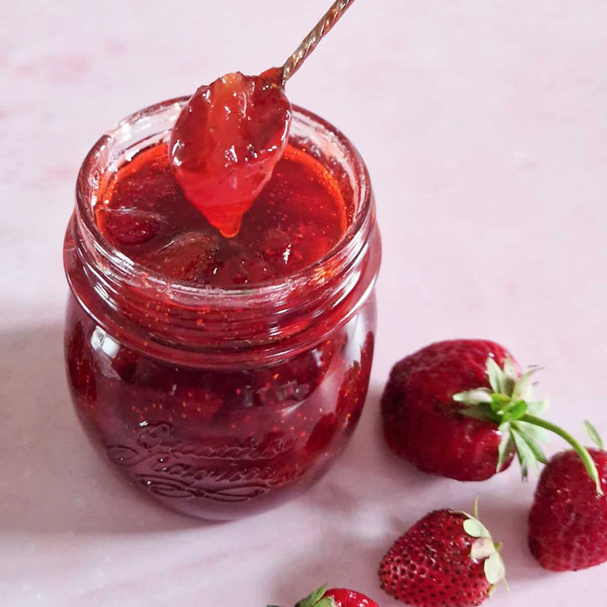 Een lepeltje aardbeienjam die uit een pot wordt gehaald.